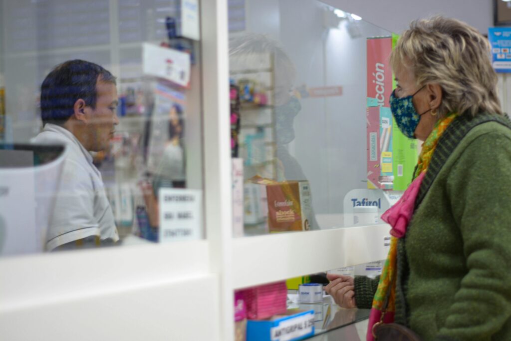 pexels photo 12332074 12332074 A woman with a mask speaks to a pharmacist behind a counter in a pharmacy.