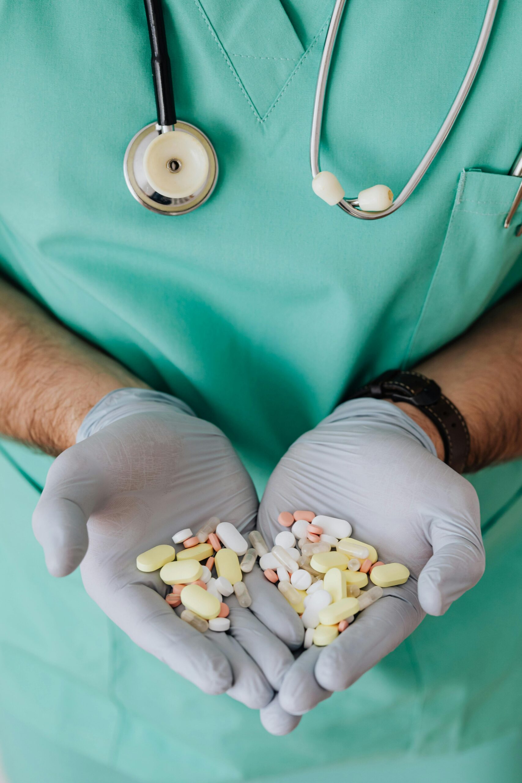 Unrecognizable man doctor wearing medical uniform and latex gloves holding pile of drugs in hands while standing in hospital and working with drugs