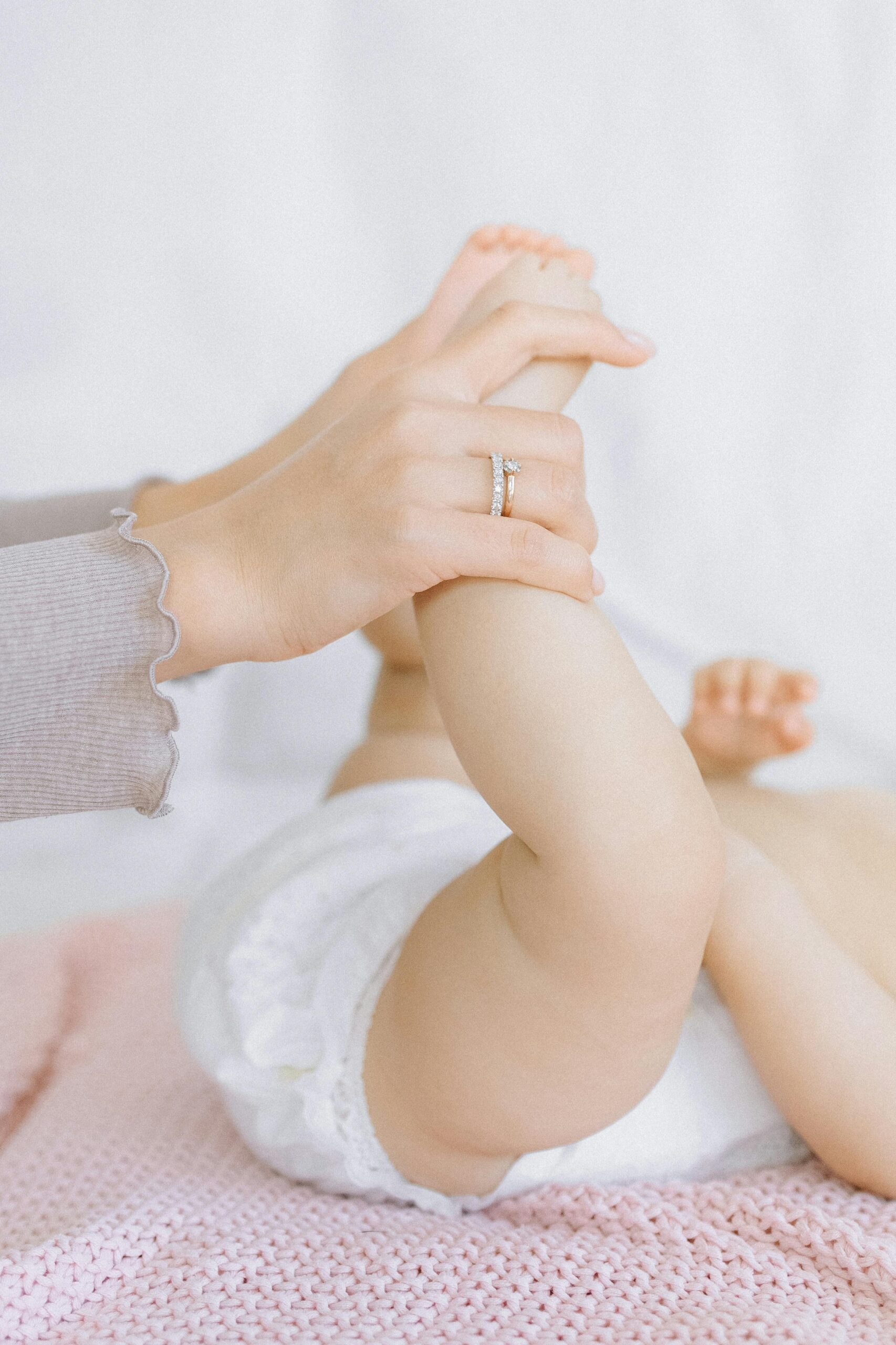 Close-up of a baby's legs being gently held by a mother's hands, symbolizing tender care.